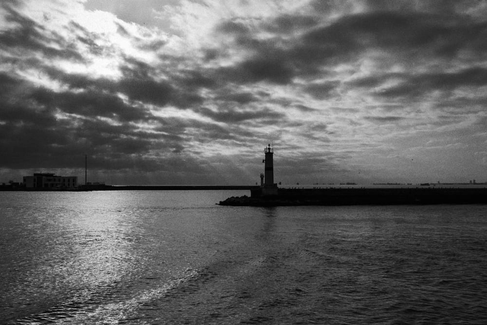 A lighthouse at the end of a breakwater under heavy cloud, in black and white.