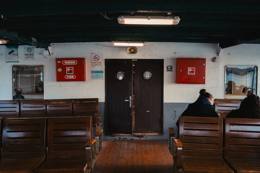 Wooden benches facing a double door inside a ferry cabin.