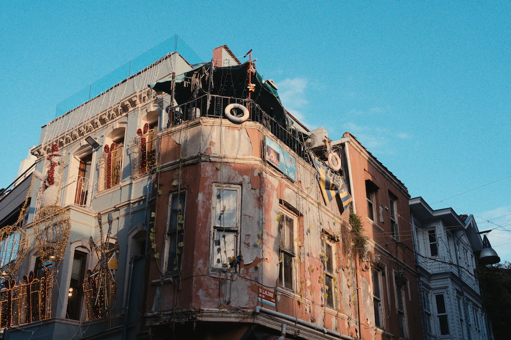 A worn pink corner building with lifebuoys on its roof terrace.