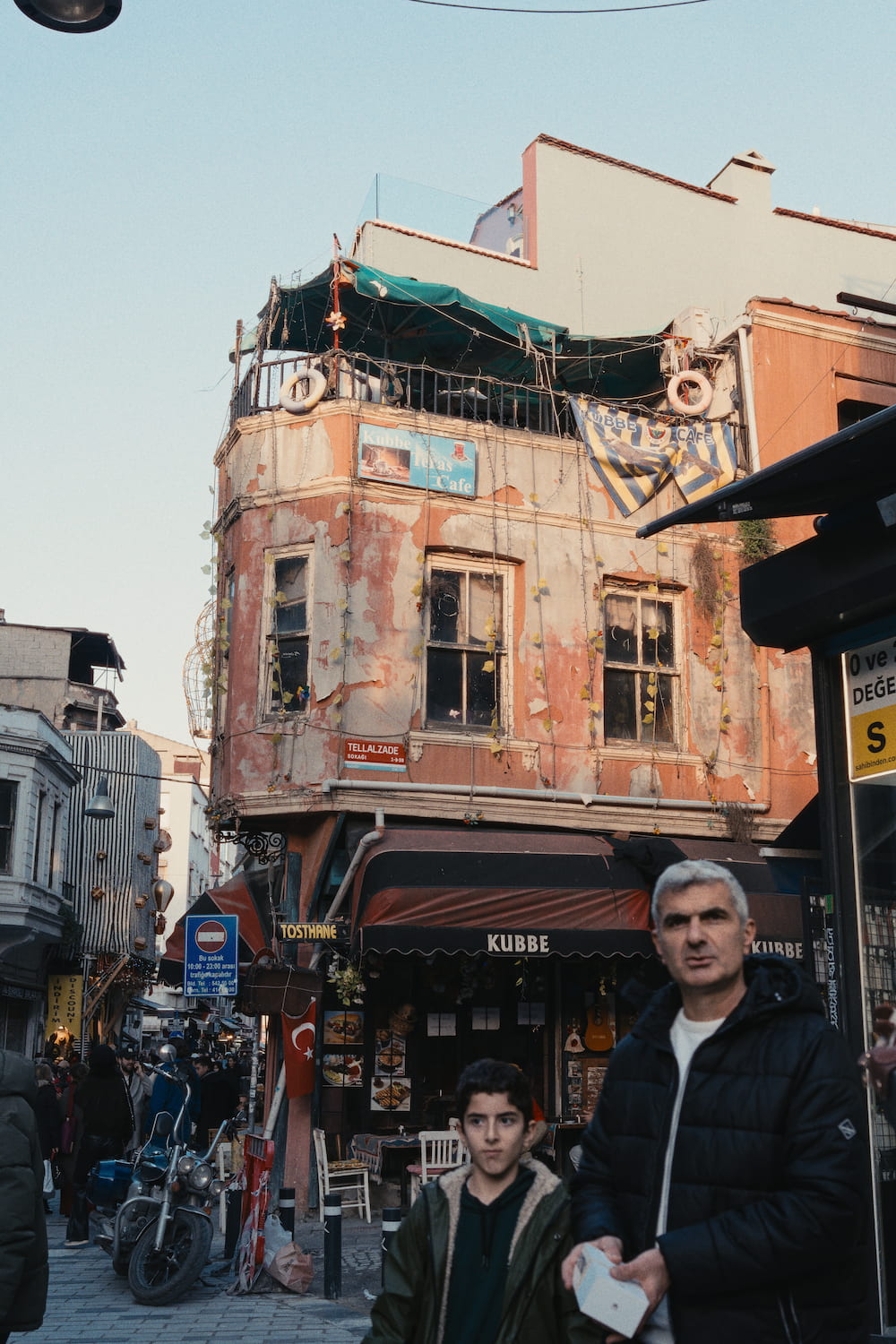 A corner building with a café over a busy street, a man and a boy walking past.