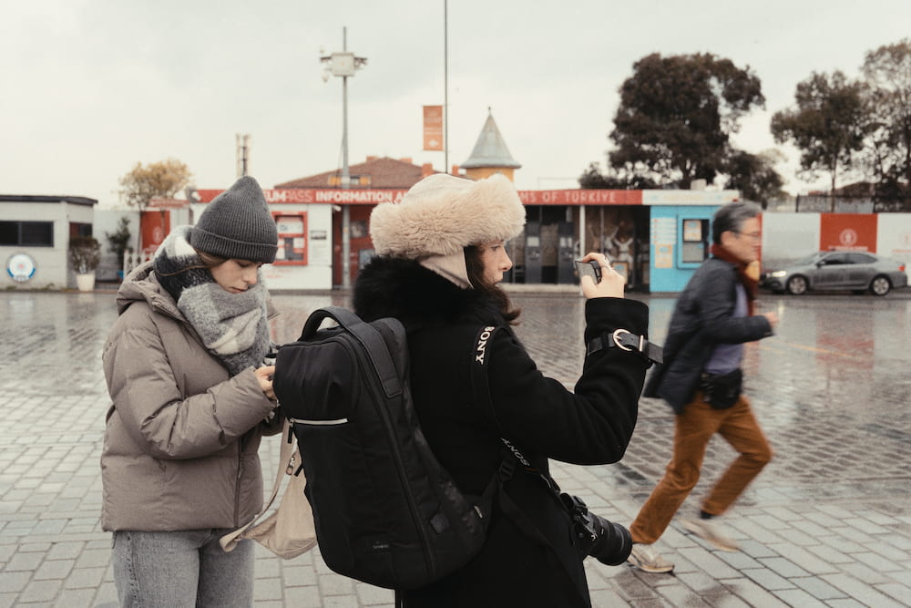 Two people taking photos on a wet square, a man walking past.