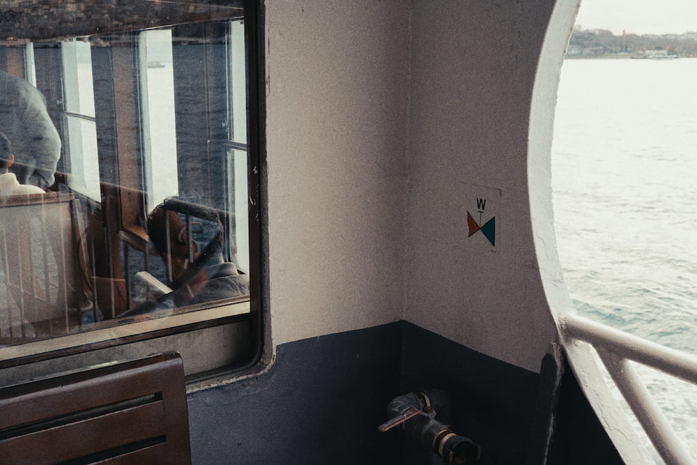 A ferry side deck with a window, a white wall and the sea through an opening.
