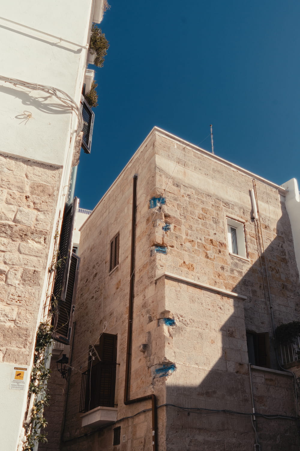 Corner of a limestone house with blue paint marks and dark shutters against a deep blue sky
