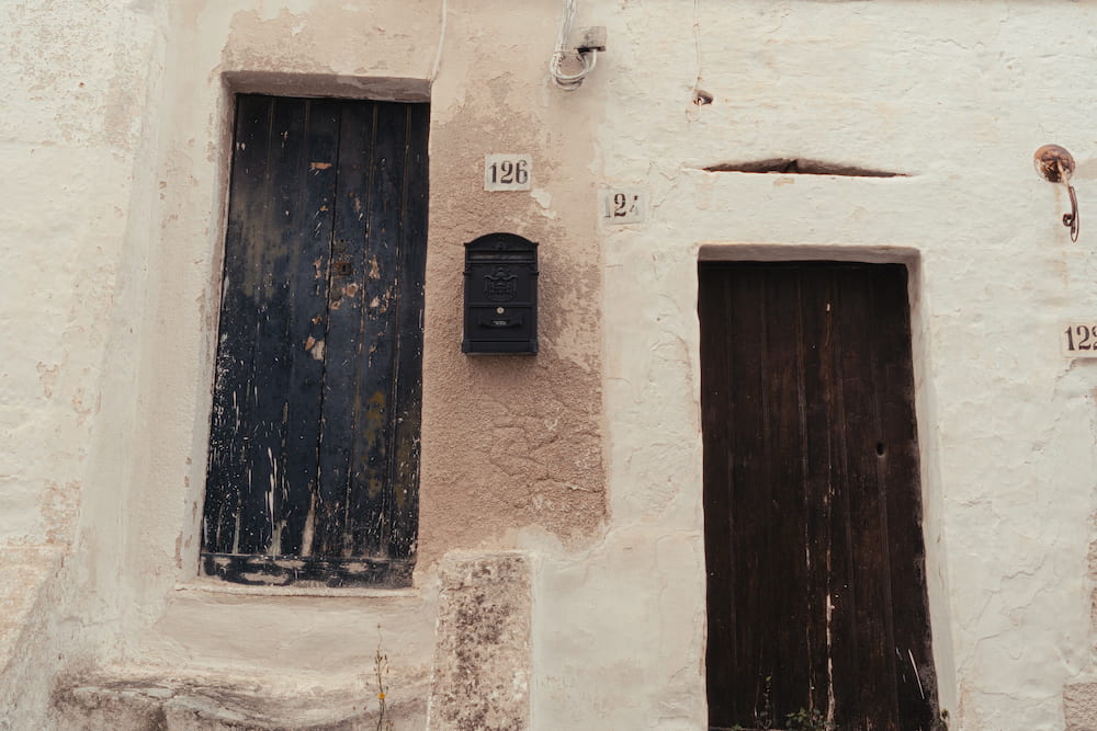 Two weathered wooden doors in a cracked whitewashed wall, numbered 126 and 124, with a black letterbox