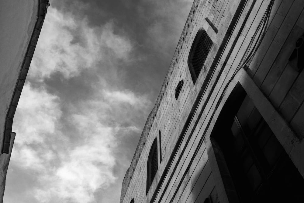 Black and white upward view of a stone facade with arched windows slanting against a cloudy sky
