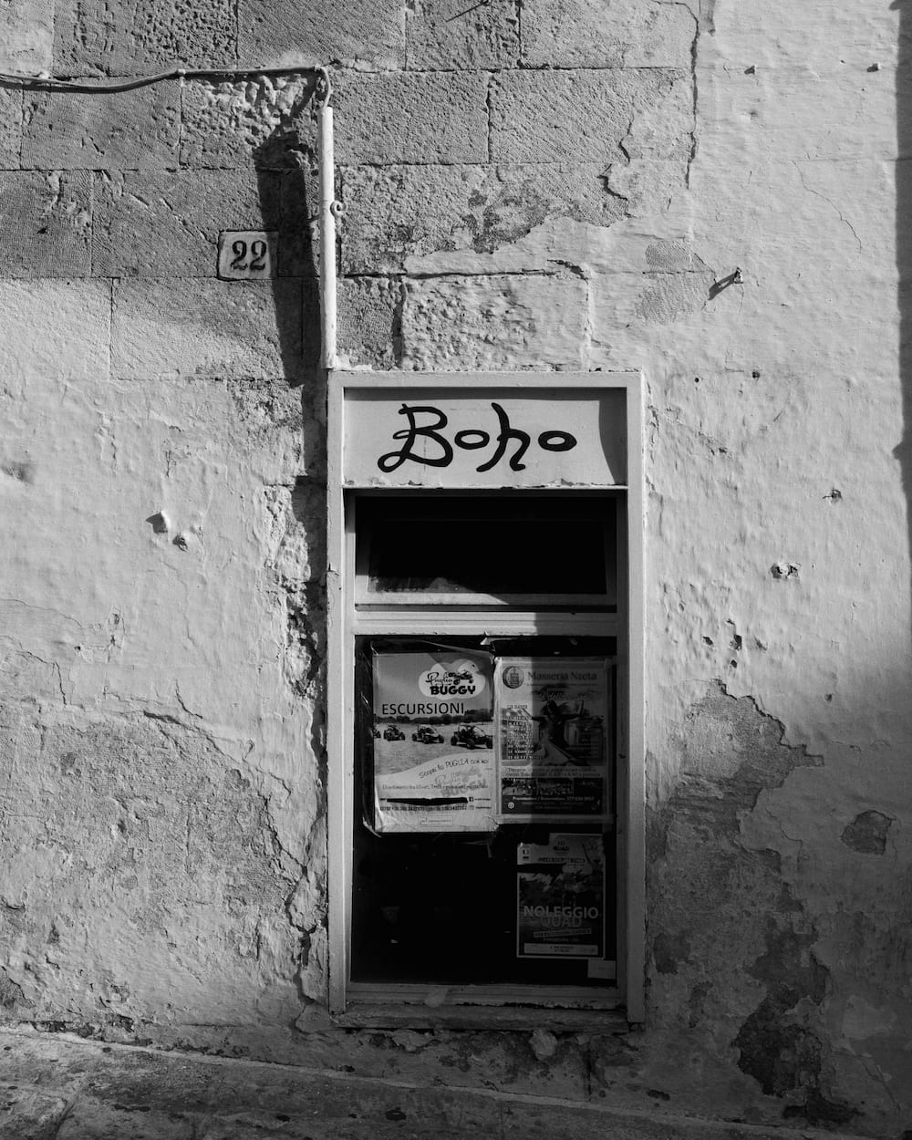 Black and white shop window signed "Boho" with tour posters, set in a cracked whitewashed wall