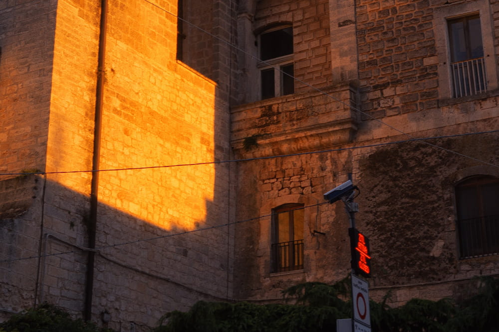 Low orange sunlight on a stone wall beside a shaded facade with a glowing red sign