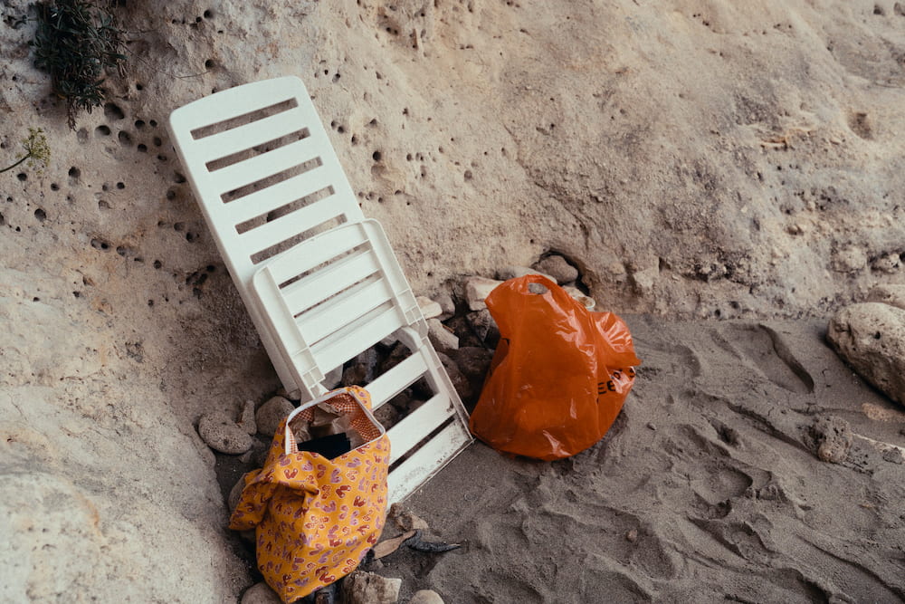 White plastic lounger leaning on a pitted rock wall beside an orange tote and an orange plastic bag