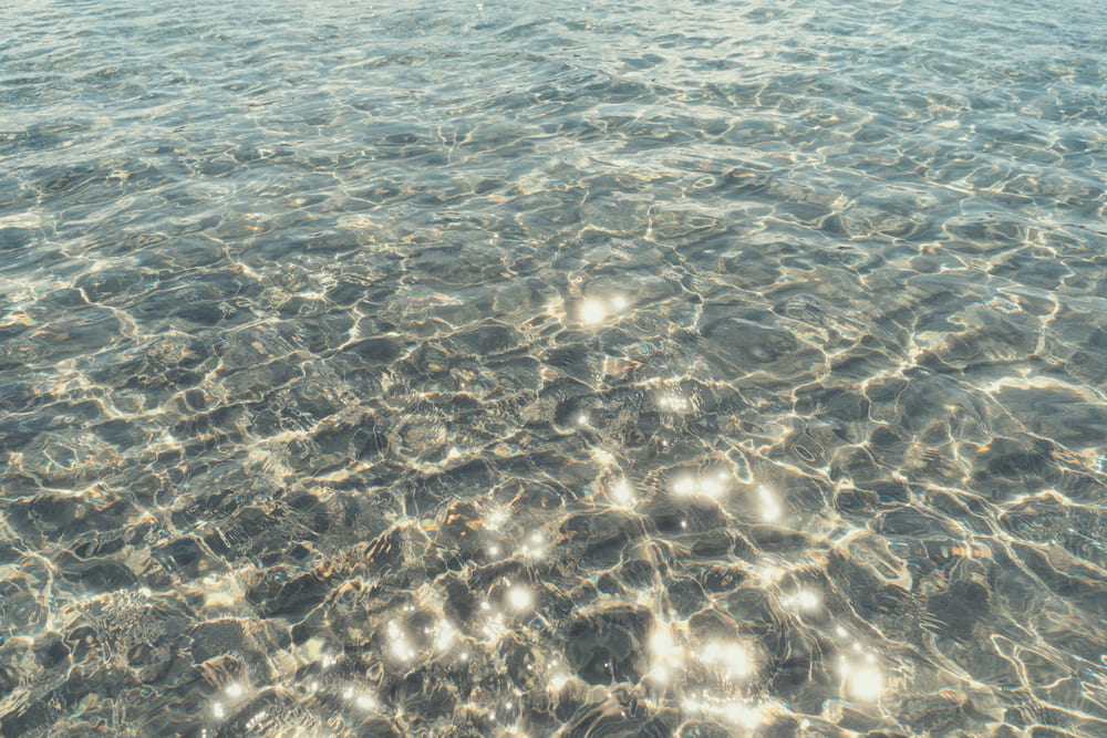 Sunlight glinting on clear shallow water over a pebbly seabed