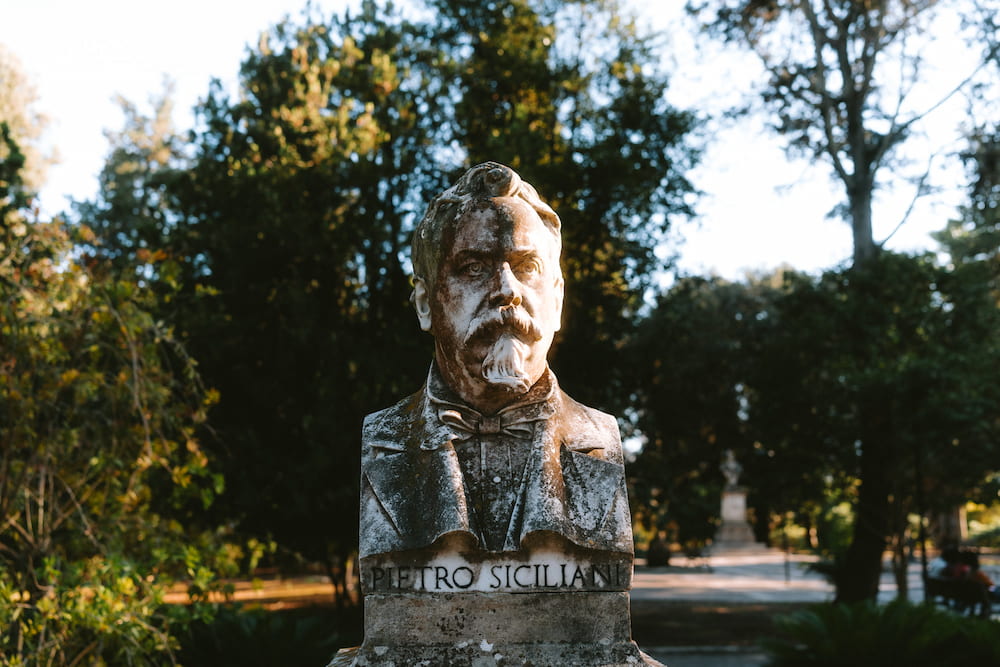 Weathered marble bust of a bearded man inscribed "PIETRO SICILIANI" in a shaded park