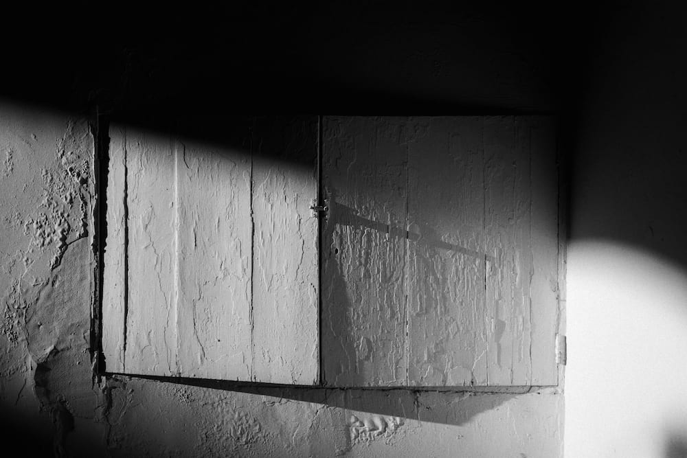 Black and white peeling wooden shutters on a rough wall, cut diagonally by sun and shadow