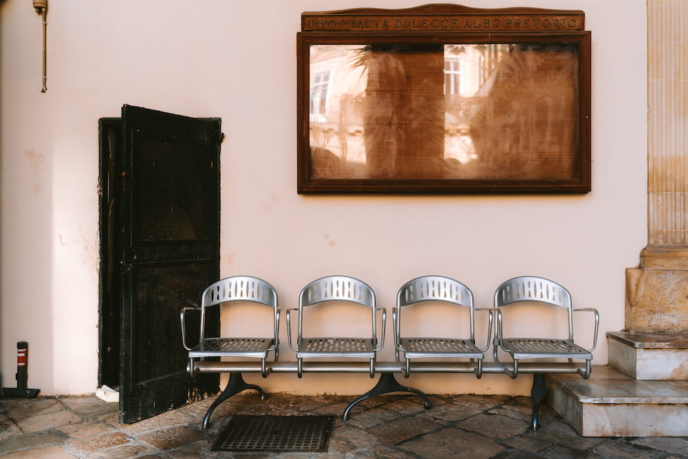 Row of four metal seats below a wooden notice board beside a half-open dark door