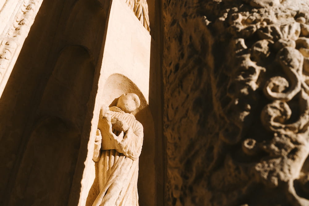 Small carved stone figure in a sunlit niche beside deeply carved ornament in shadow