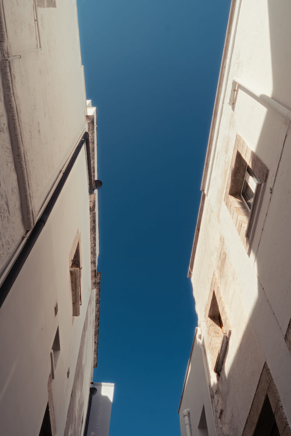 Looking straight up between two whitewashed walls at a narrow strip of deep blue sky