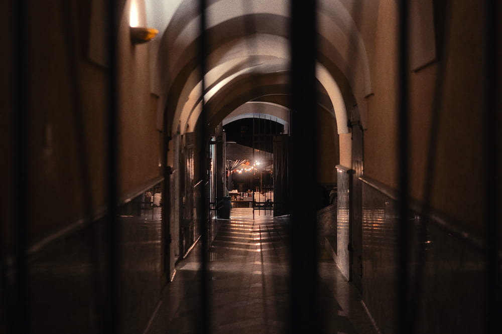 A vaulted arcade at night, lamps reflected on the floor, seen past dark pillars