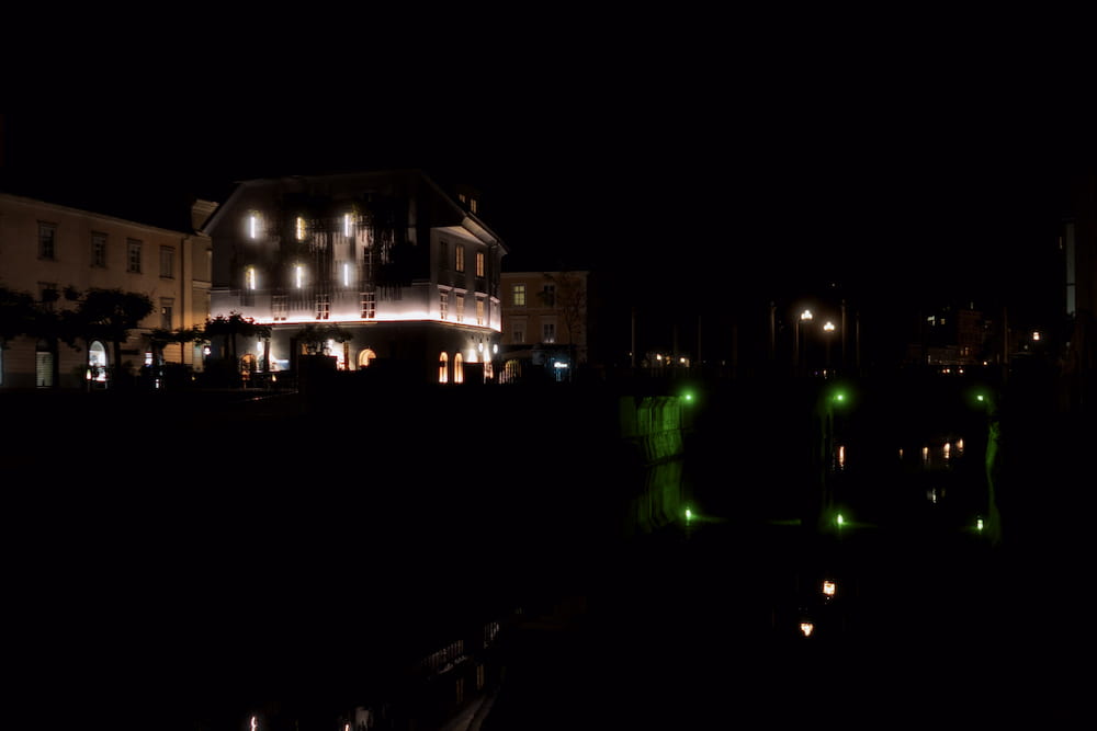 A lit hotel across dark water, small green lights reflected below
