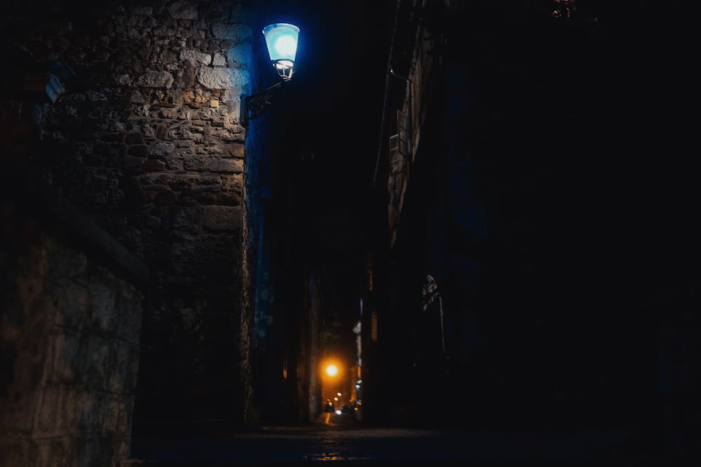 A stone wall under a blue street lamp, an orange light far down a dark passage