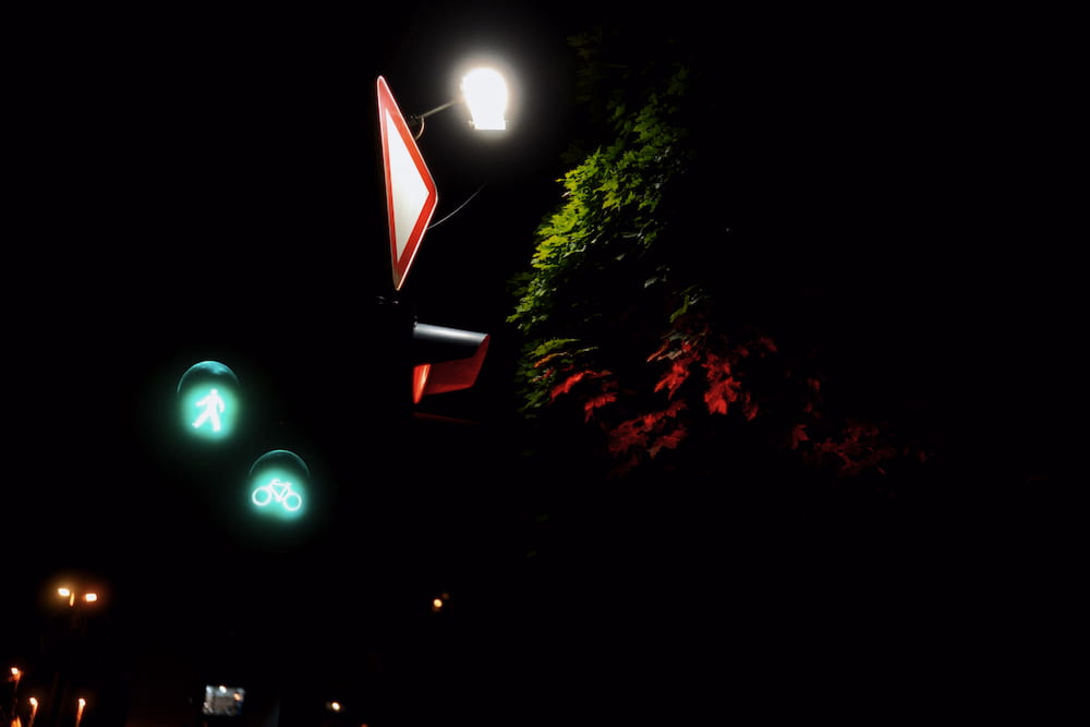 A yield sign under a street lamp, green crossing lights and red leaves in the dark