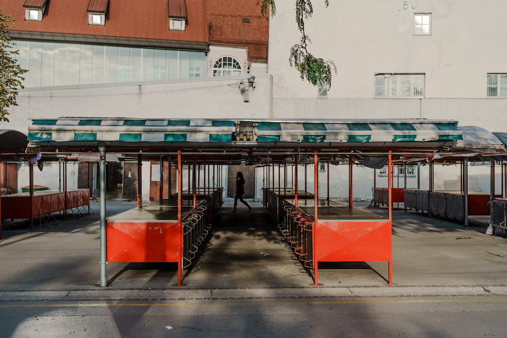 Empty red market stalls under green and white striped awnings, a white building behind