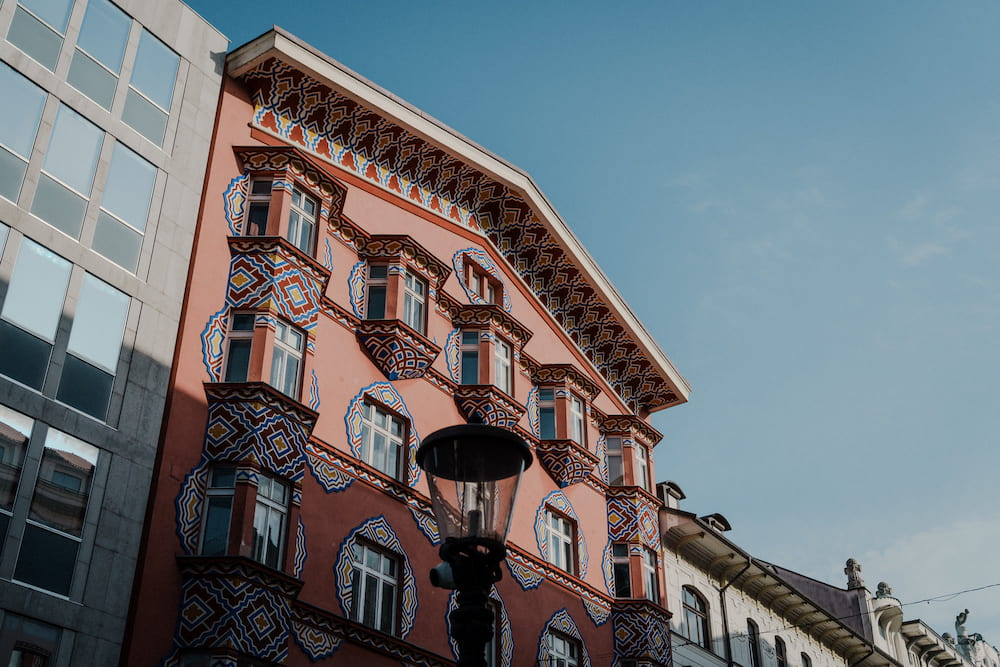 The pink patterned building from its corner beside a glass building, blue sky