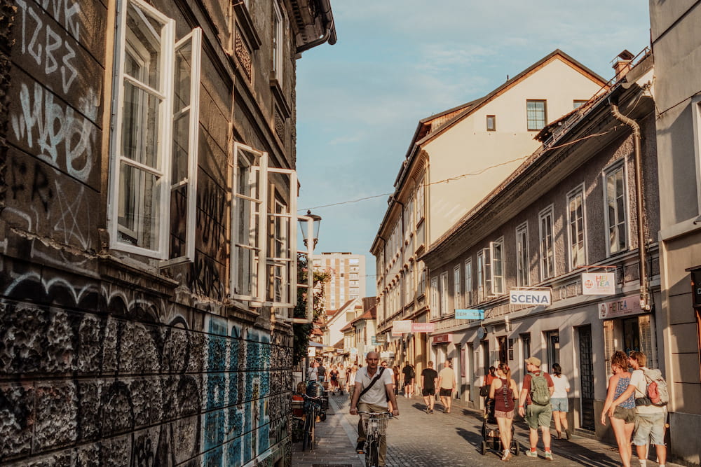 A street with graffiti-covered walls and open windows, people walking