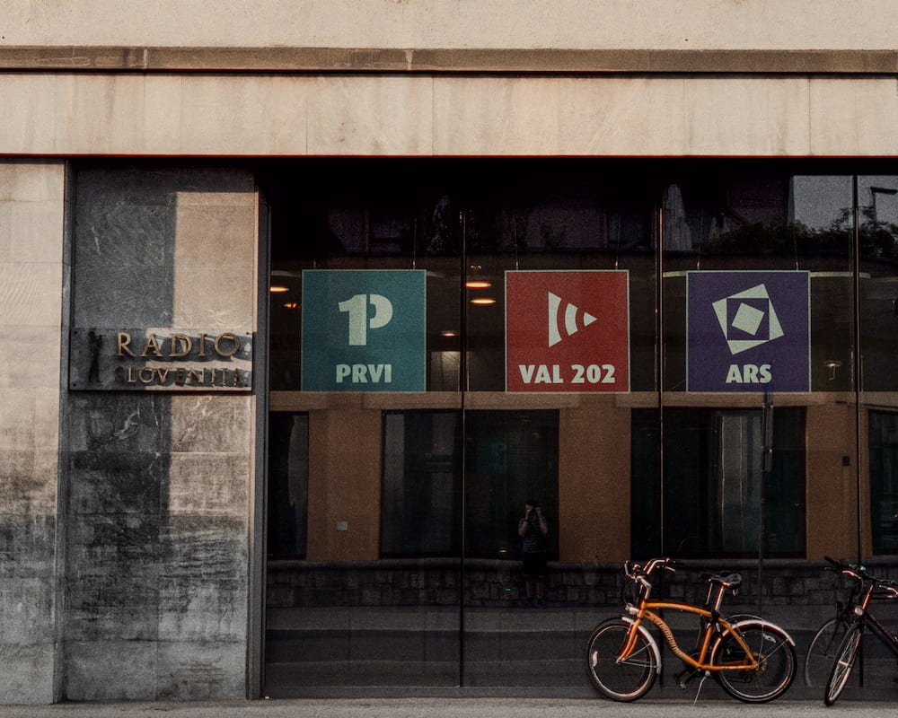 A concrete entrance with three radio station signs, orange bicycles parked in front