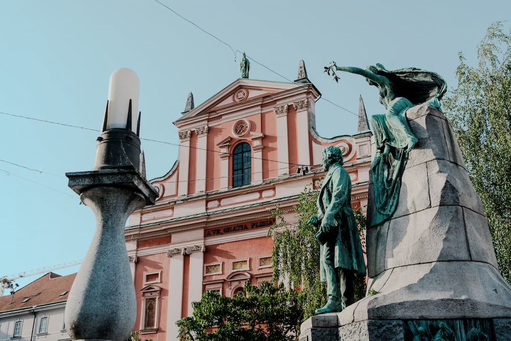 A pink church front behind a bronze statue and a lamp post
