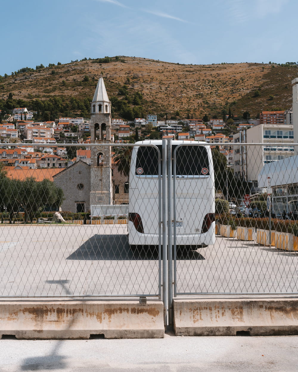 A white coach parked behind a fence, a town and a bell tower on the hill behind.
