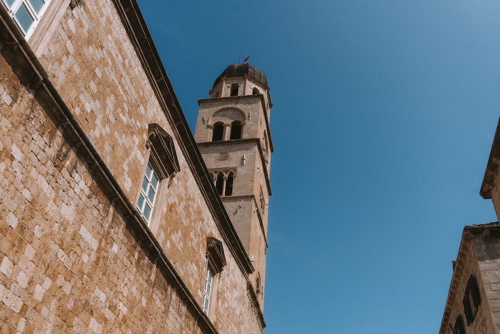 Looking up at a stone street and a bell tower against a blue sky.