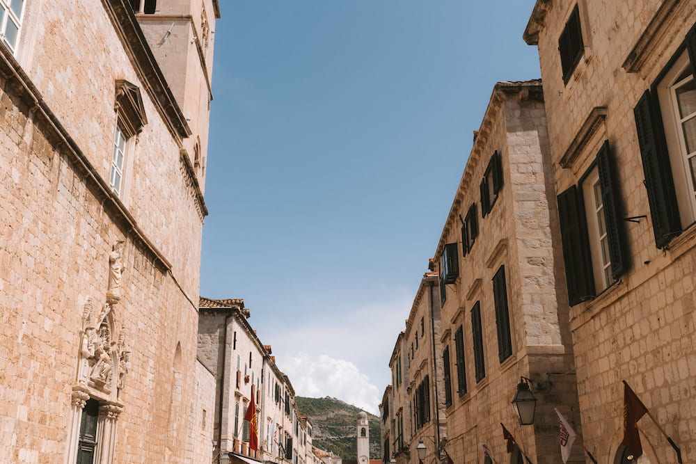 Looking up along a street of stone houses with green shutters.