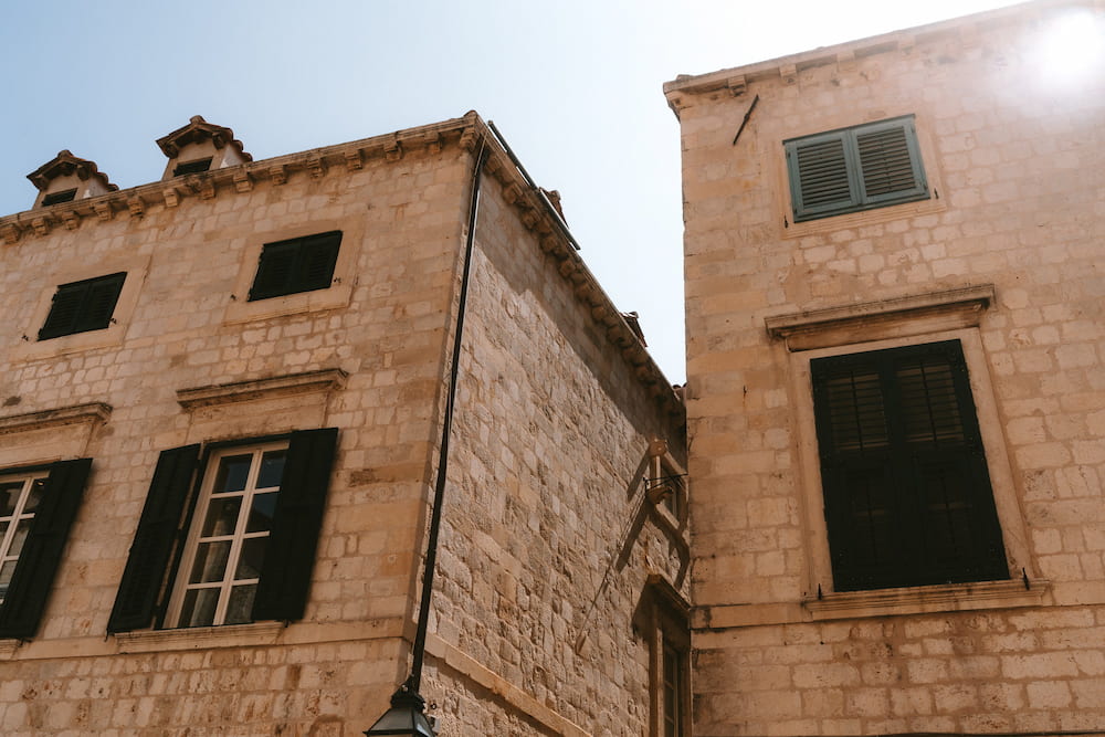 Stone houses with green shutters in bright sun.