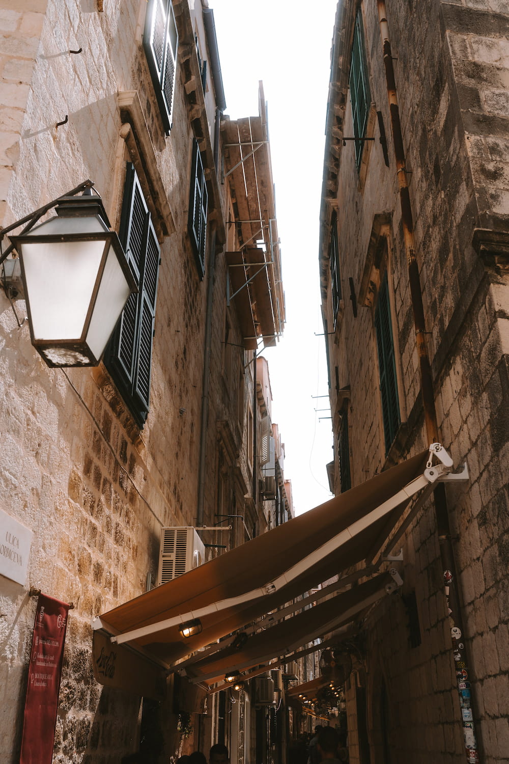 A lantern and awnings in a narrow stone lane, looking up.