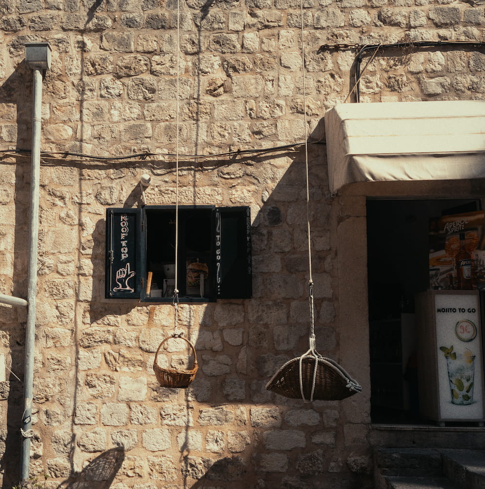 A stone wall with a small shop window, hanging baskets and an awning.