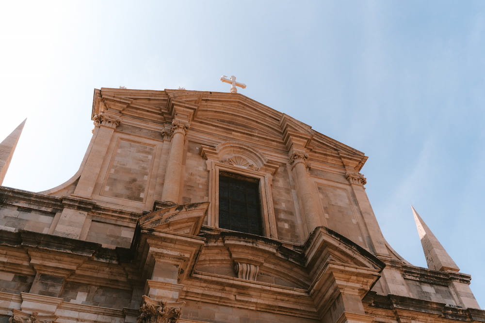 A baroque church front with a cross, seen from below.