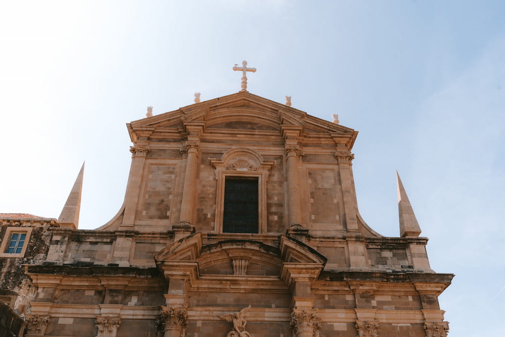 A baroque church front with a cross against a pale sky.