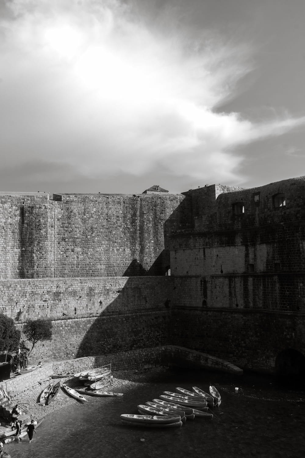 Black and white: city walls over a small cove with kayaks.