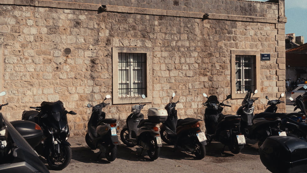 Black and grey scooters parked against a stone wall.