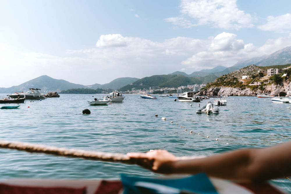 A hand holding a rope on a boat, boats and green hills on the water.