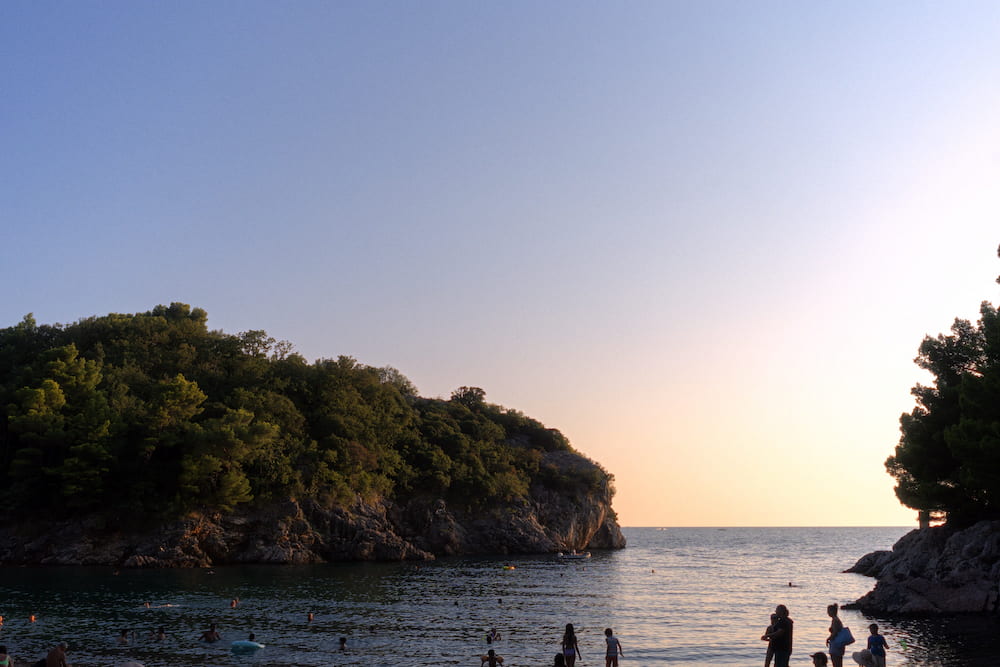 A wooded headland over a cove at sunset, people at the water.
