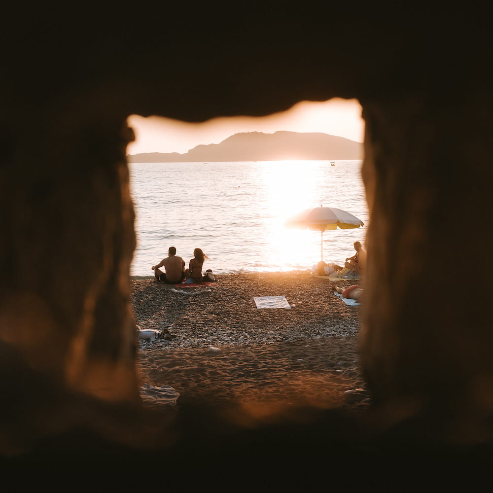 A beach and the sunset sea seen through a square hole in a stone wall, darker.