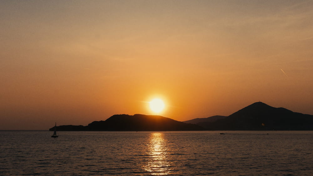 The sun setting over the sea behind an island.