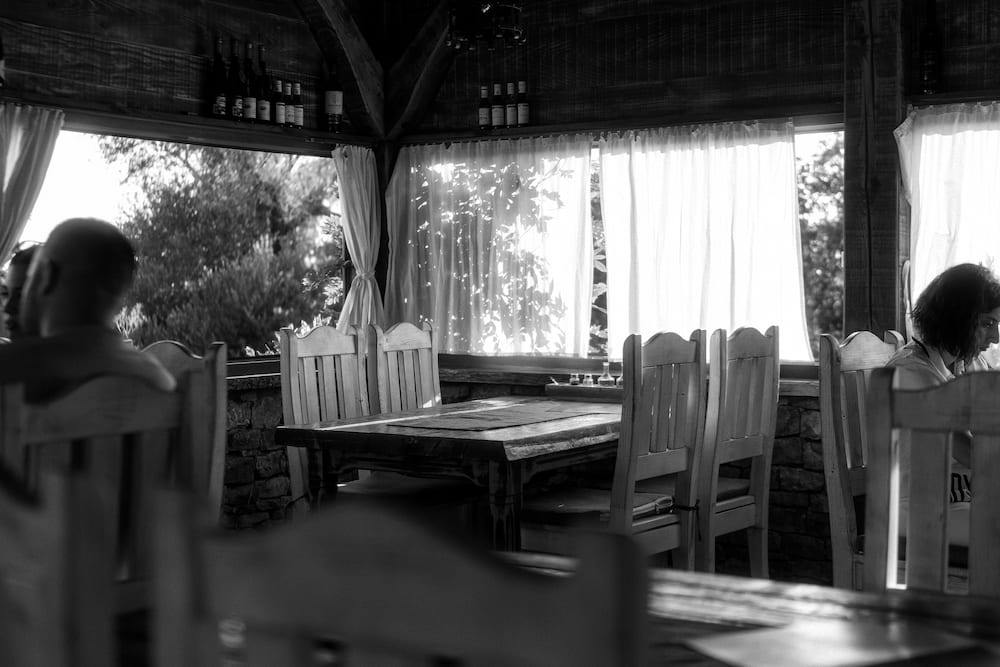 Black and white: wooden chairs and tables in a konoba, sun through white curtains