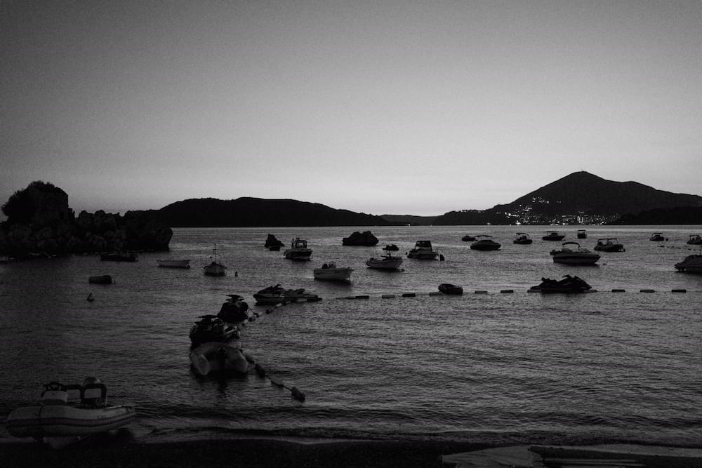 Black and white: boats moored in the bay at dusk, hills beyond