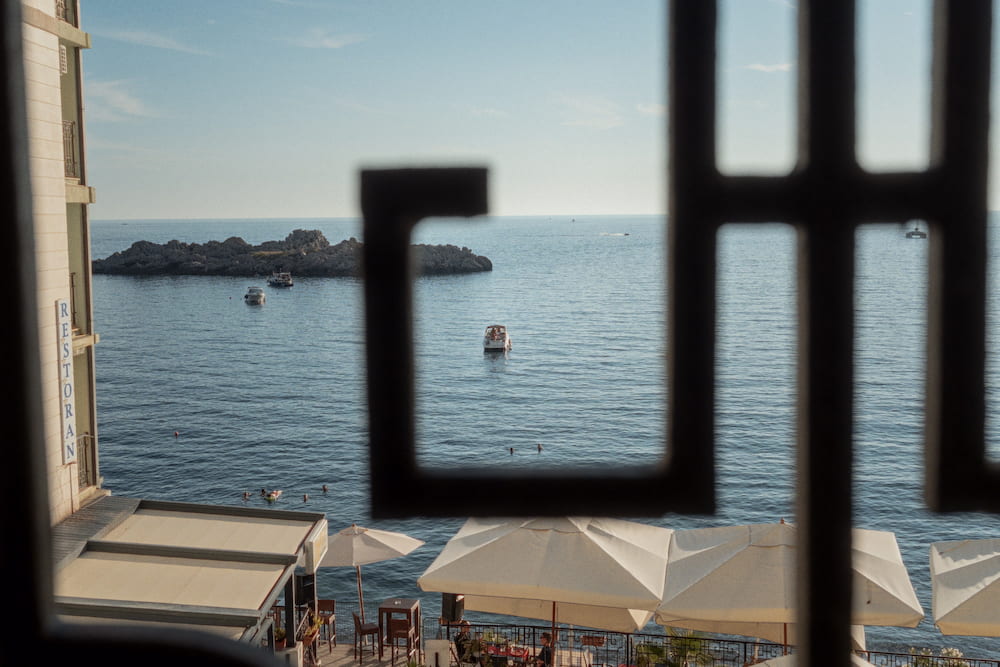 The sea through a black iron window grille, beach parasols below