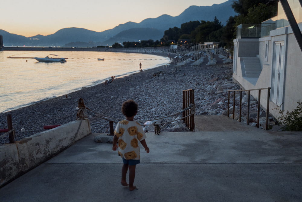 A small child walking towards a pebble beach at dusk