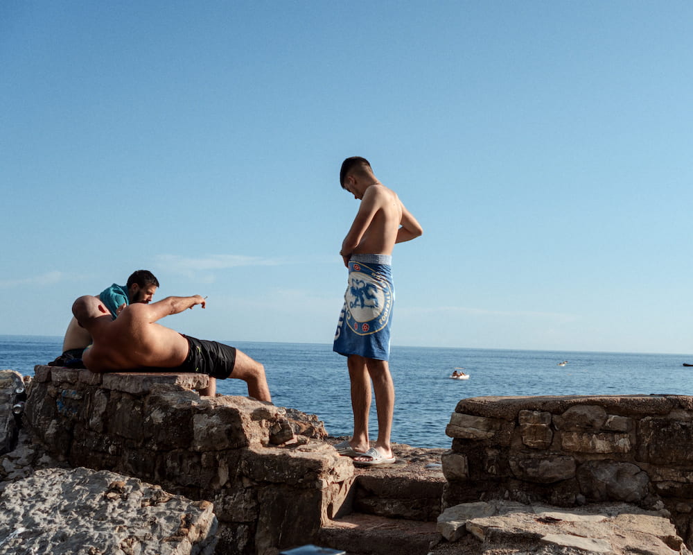 Two men on rocks by the sea, one pointing
