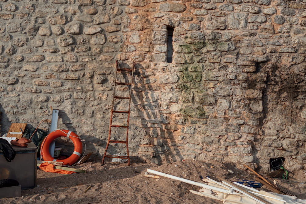 A ladder, a life ring and clutter against an old stone wall