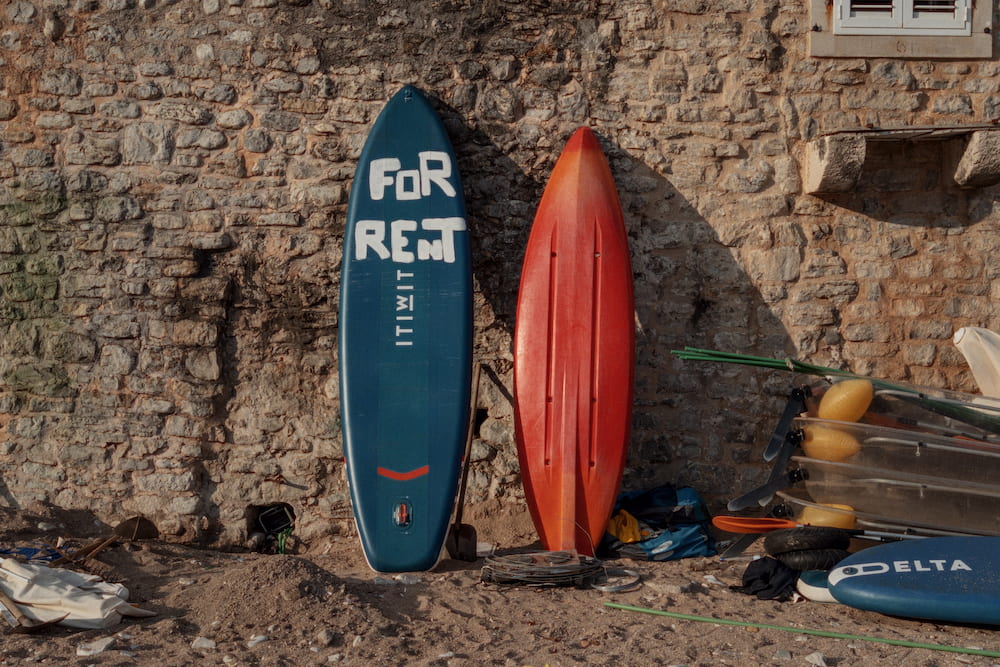 Two paddle boards marked For Rent against a stone wall