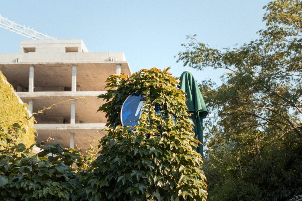 An unfinished building behind trees and a round road mirror