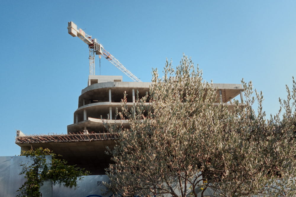 A crane over an unfinished building behind an olive tree